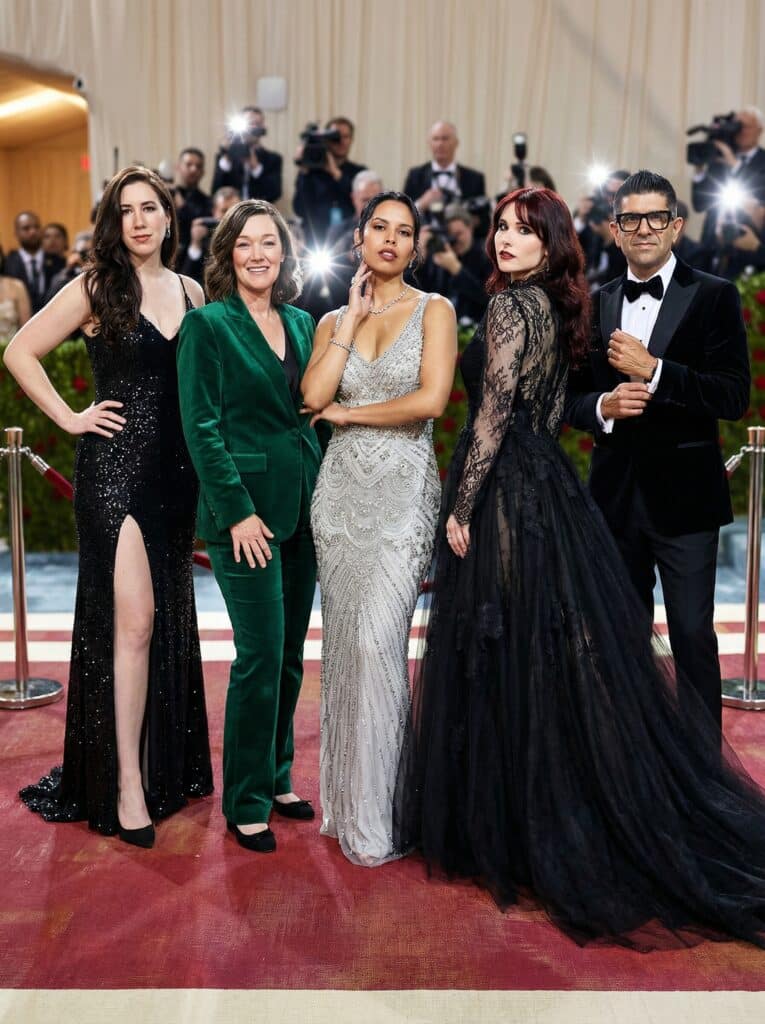 Group of elegantly dressed individuals posing on the red carpet at the Met Gala, showcasing high-fashion styles and luxury aesthetics, surrounded by photographers capturing the moment.