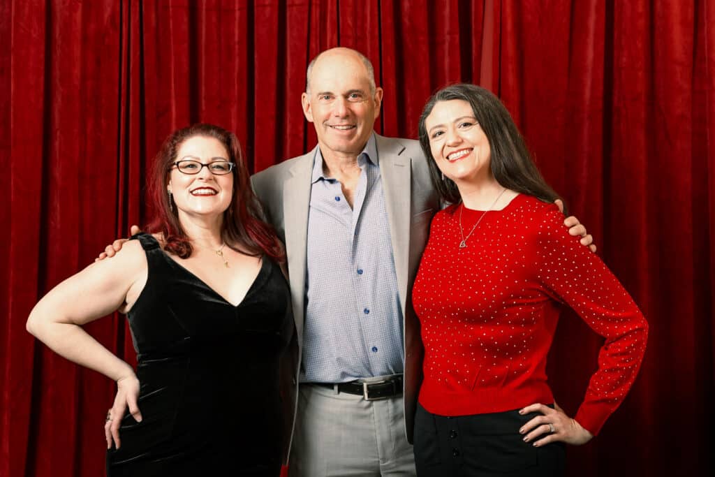 Group of three smiling individuals posing together in front of a rich red velvet backdrop, showcasing a sophisticated photo booth setting ideal for upscale events and celebrations.