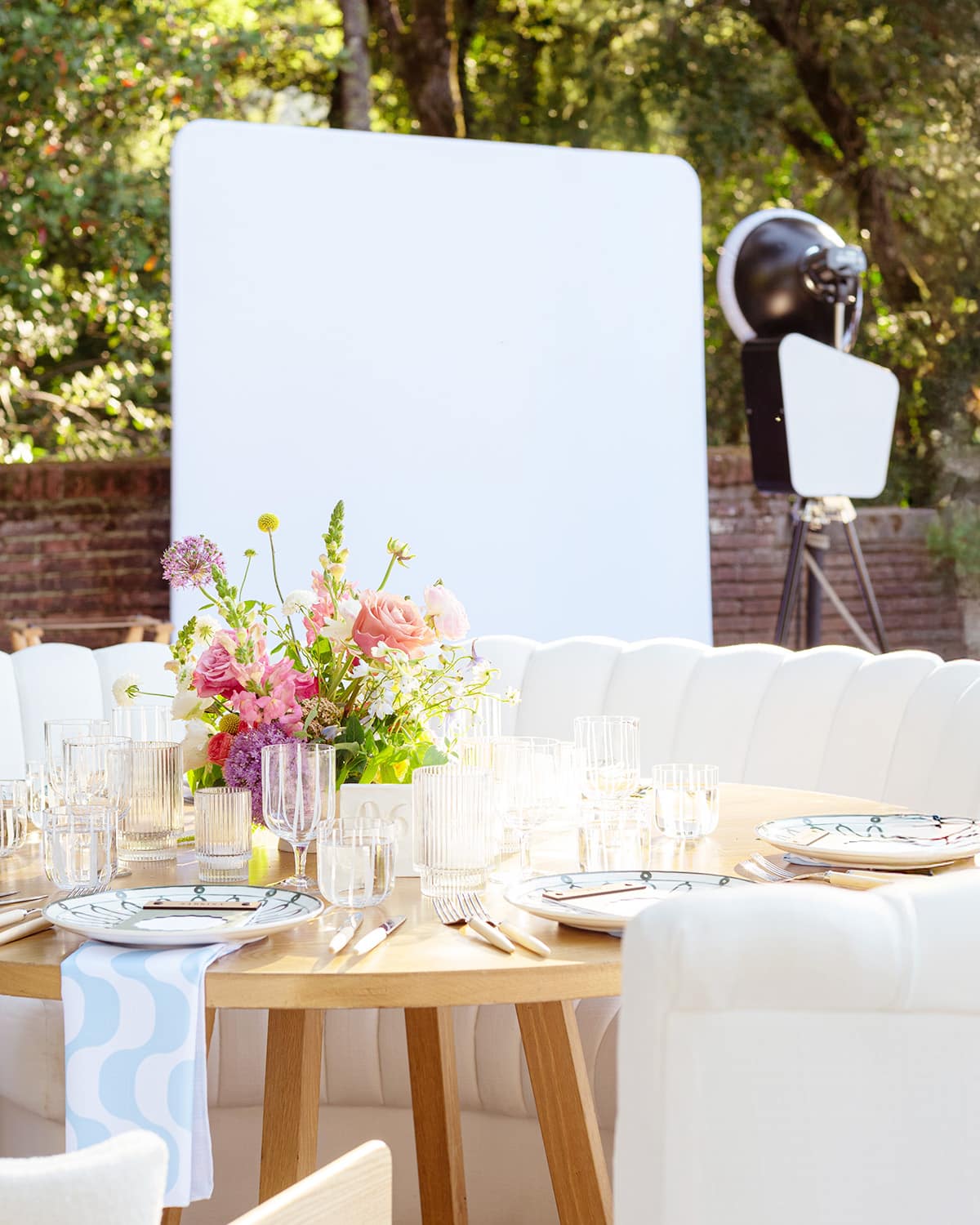 Elegant wedding table setting with floral centerpiece, glassware, and dinnerware, featuring a photo booth backdrop in a lush outdoor setting.