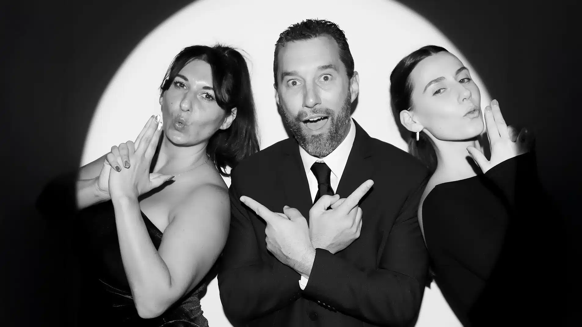 Group posing dramatically in black and white, showcasing playful expressions and stylish attire, highlighting the engaging atmosphere of the Spotlight Booth experience.