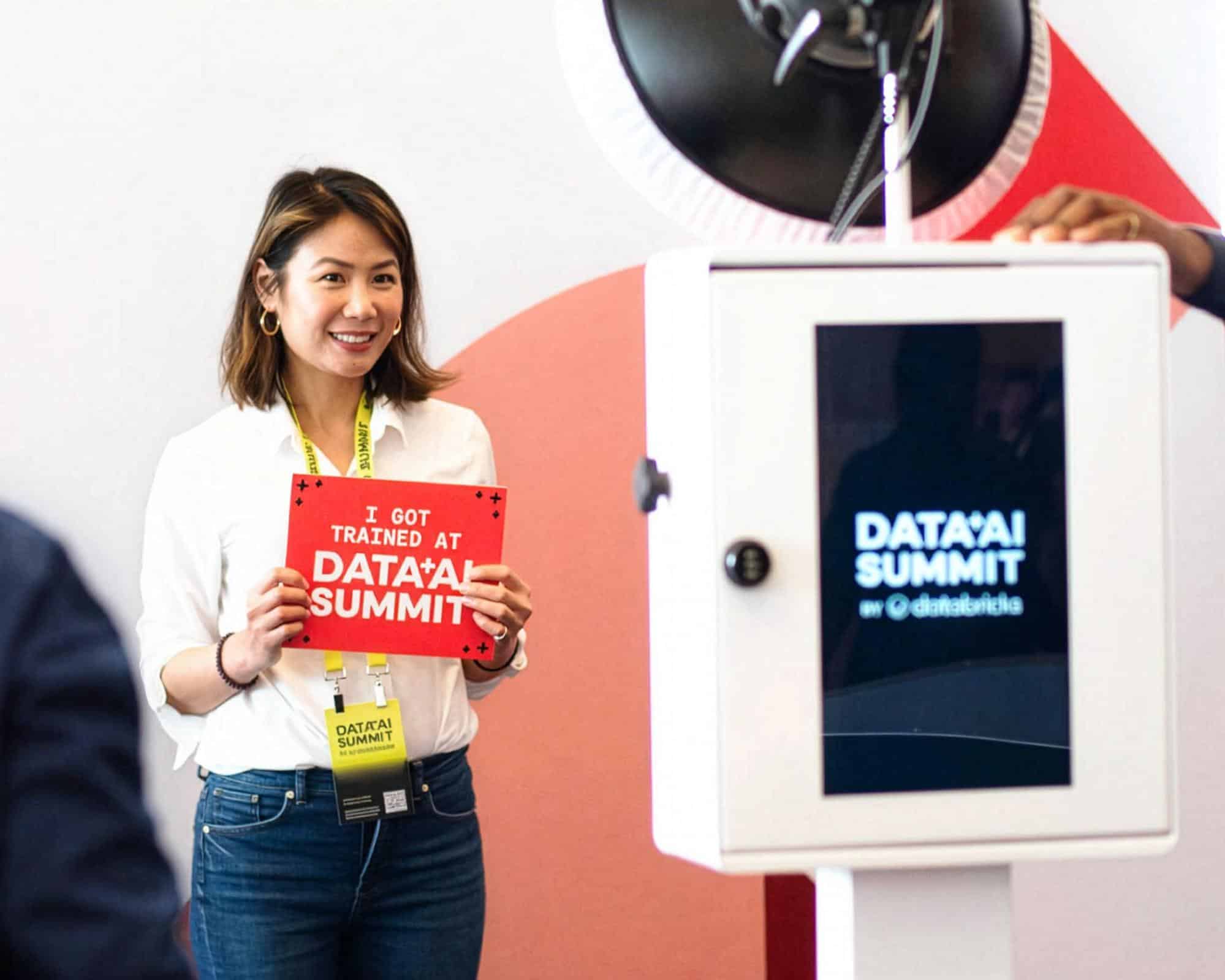 Woman smiling and holding a sign that says "I GOT TRAINED AT DATA*A*I SUMMIT" next to a branded photo booth displaying the event logo, capturing a moment of engagement at a corporate event.
