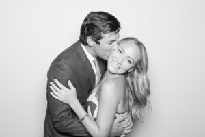 Couple embracing and sharing a kiss in a playful photo booth setting, capturing a joyful and intimate moment, reflecting the essence of love and shared experiences at events like weddings or anniversaries.