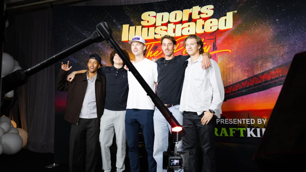 Group of five young men posing together at the Sports Illustrated Super Bowl Party, with a vibrant backdrop featuring the event logo and branding, highlighting the festive atmosphere of the occasion.