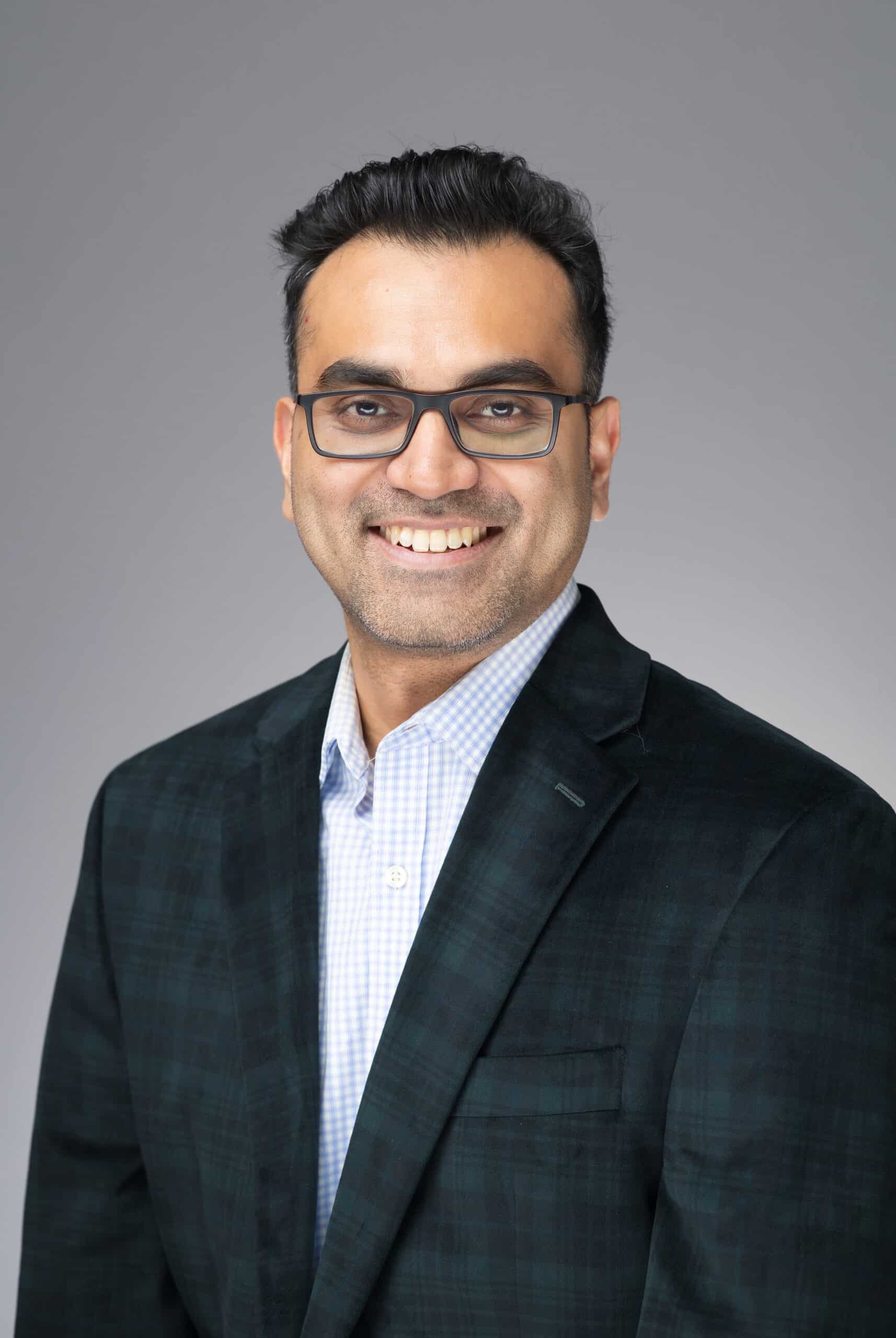 Professional headshot of a smiling man in a dark blazer and checkered shirt, showcasing confidence and approachability, reflecting Pop Life Photo's high-quality photography services for corporate events and personal portraits.