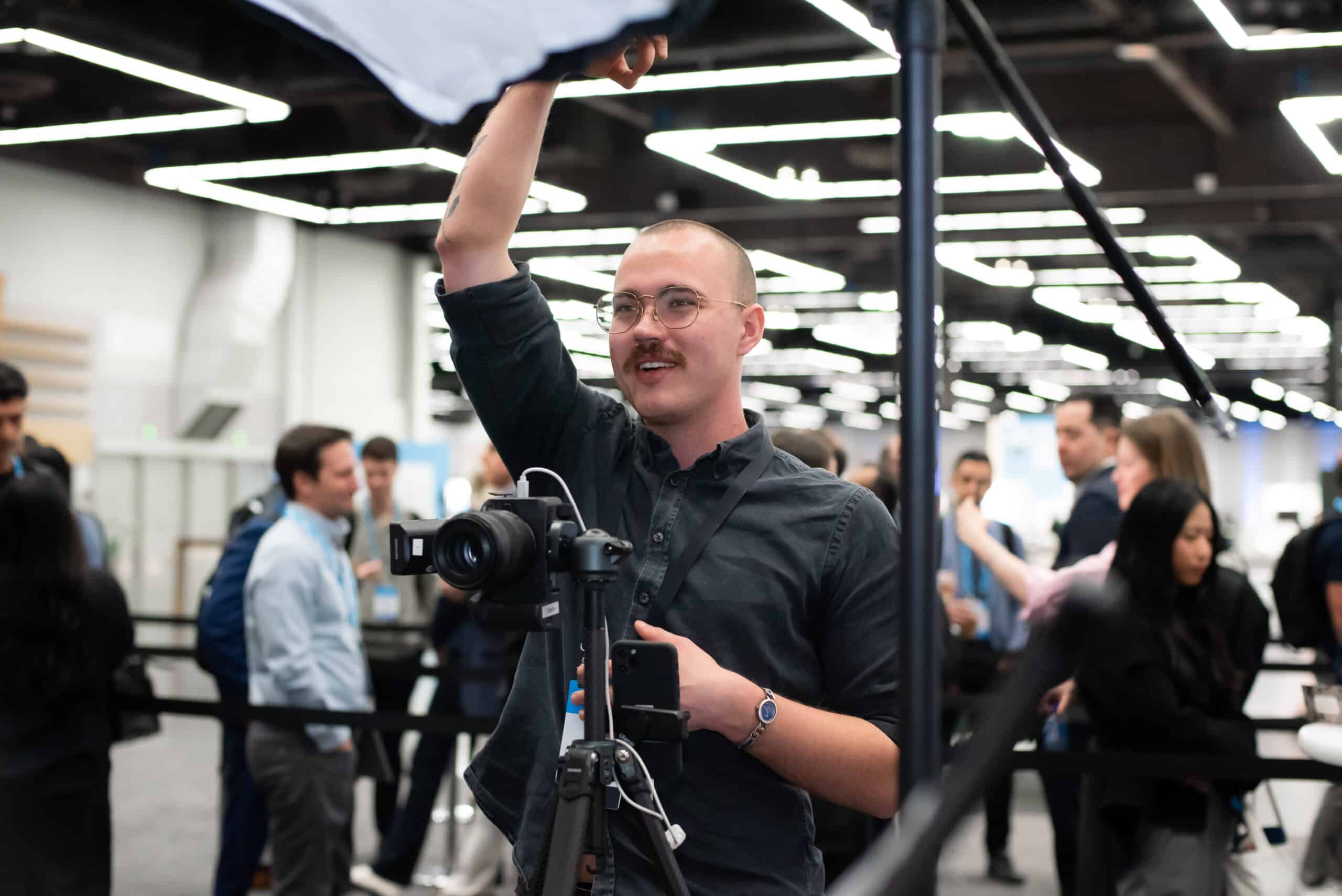 Photographer adjusting lighting setup for professional headshots at a corporate event, with guests in the background engaged in conversation.