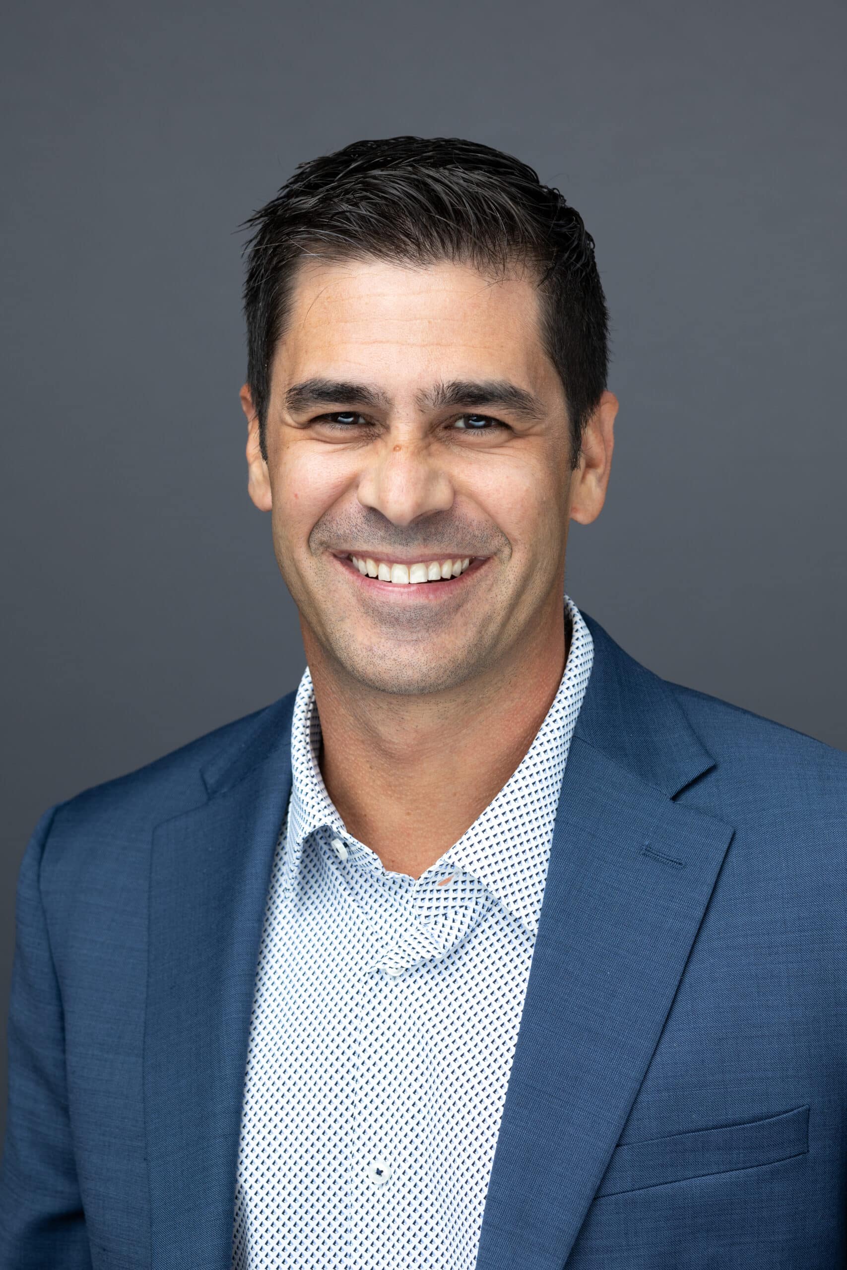 Professional male headshot featuring a smiling man in a blue suit and patterned shirt, showcasing confidence and approachability, ideal for corporate branding and event photography.
