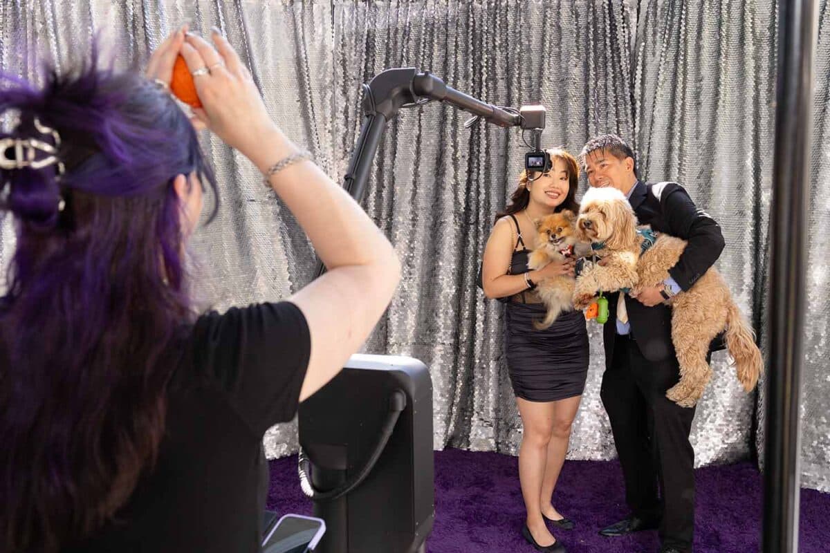 Couple posing with two dogs in a stylish photo booth at the Fur Ball event, with a sparkling backdrop and vibrant purple carpet, capturing glamorous moments for guests and their pets.