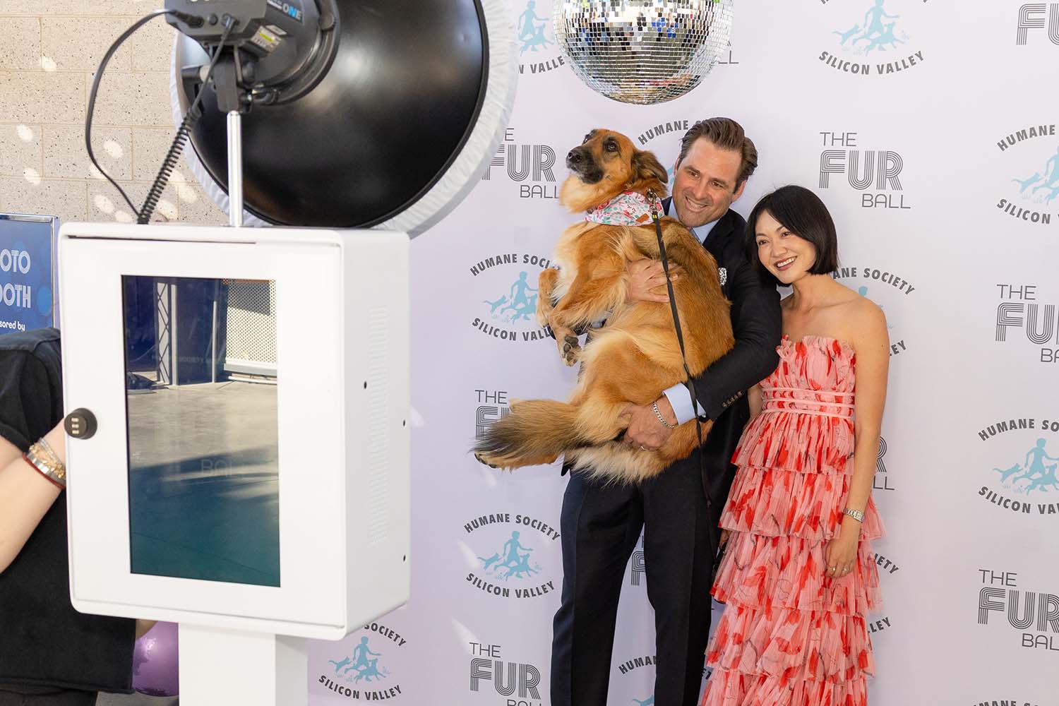 Guests posing with a dog in front of a photo booth at The Fur Ball event, featuring a disco ball and branding for the Humane Society Silicon Valley.