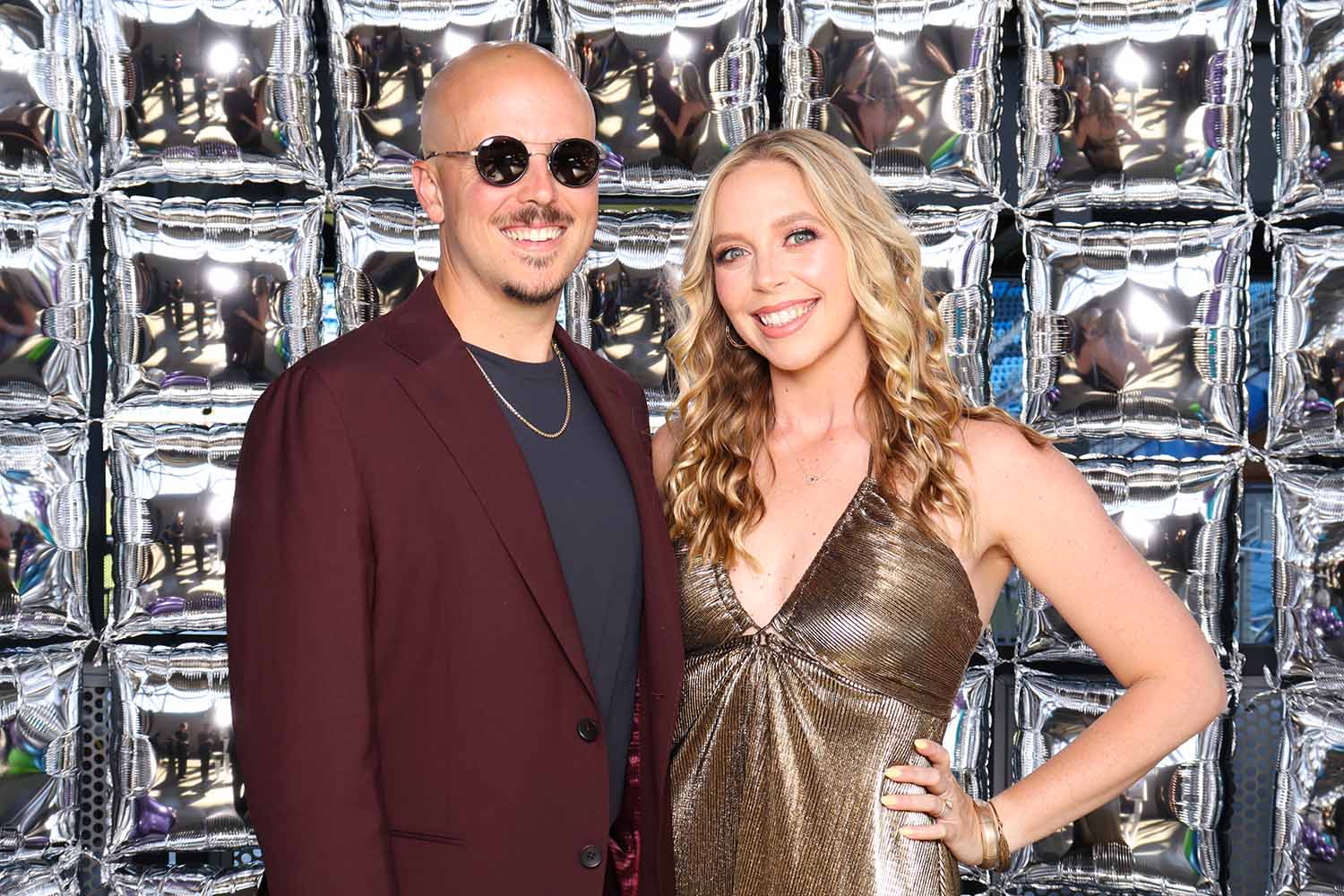 Couple posing in glamorous attire against a shiny silver backdrop, capturing stylish moments at the Fur Ball event supporting the Humane Society Silicon Valley.