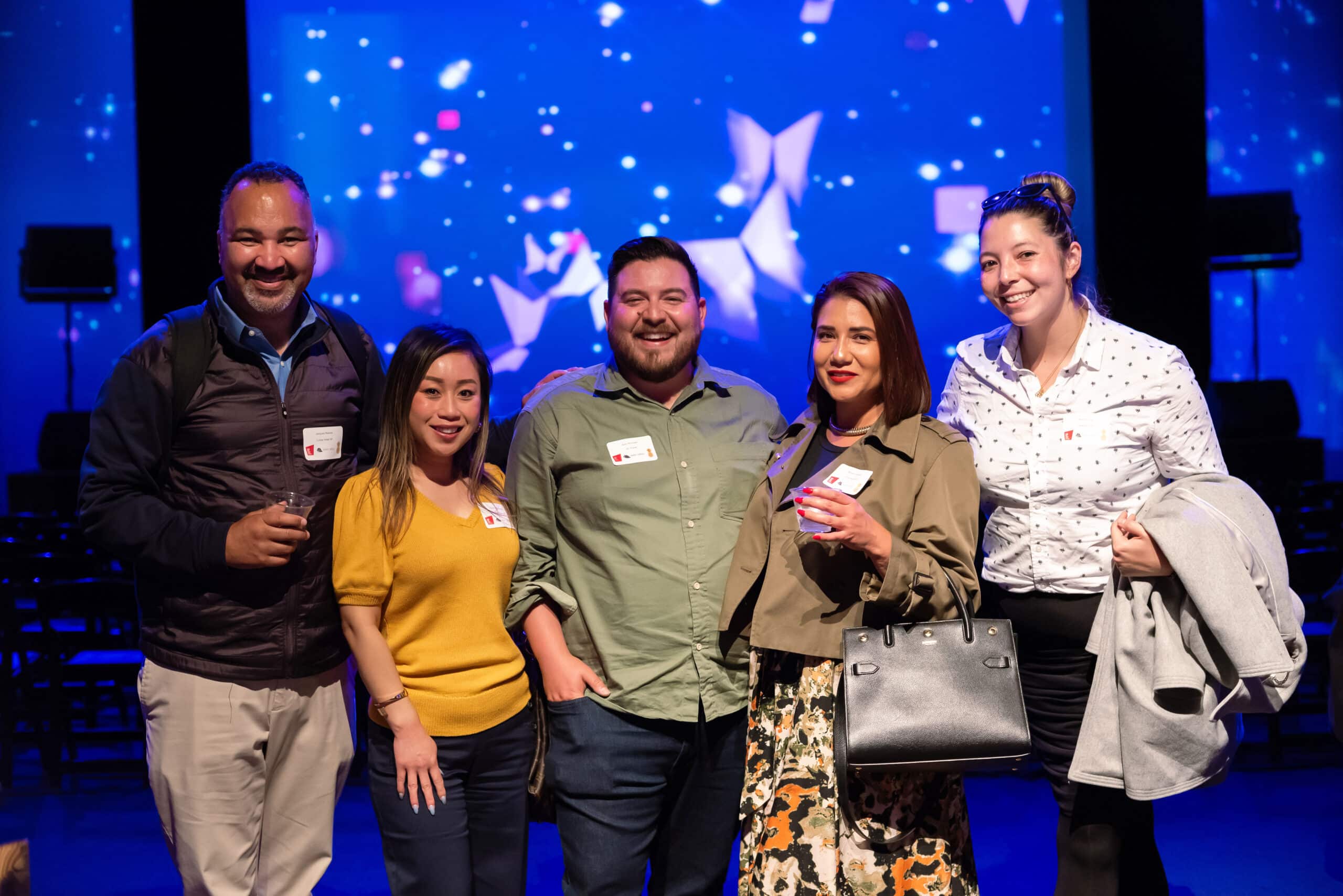 Group of five smiling guests at a lively event, with a colorful backdrop, showcasing engagement and camaraderie, highlighting Pop Life Photo's event photography service.