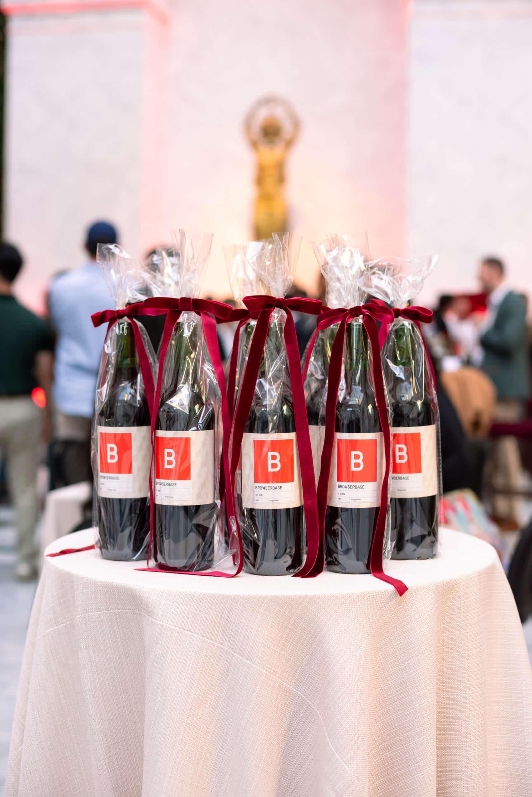 Bottles of wine elegantly wrapped with red ribbons and branded labels on a table, enhancing guest engagement at a corporate event.