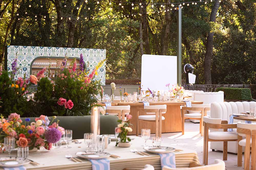 Elegant outdoor wedding setup at Filoli, featuring floral centerpieces, wooden tables, and a glam photo booth backdrop, illuminated by string lights.