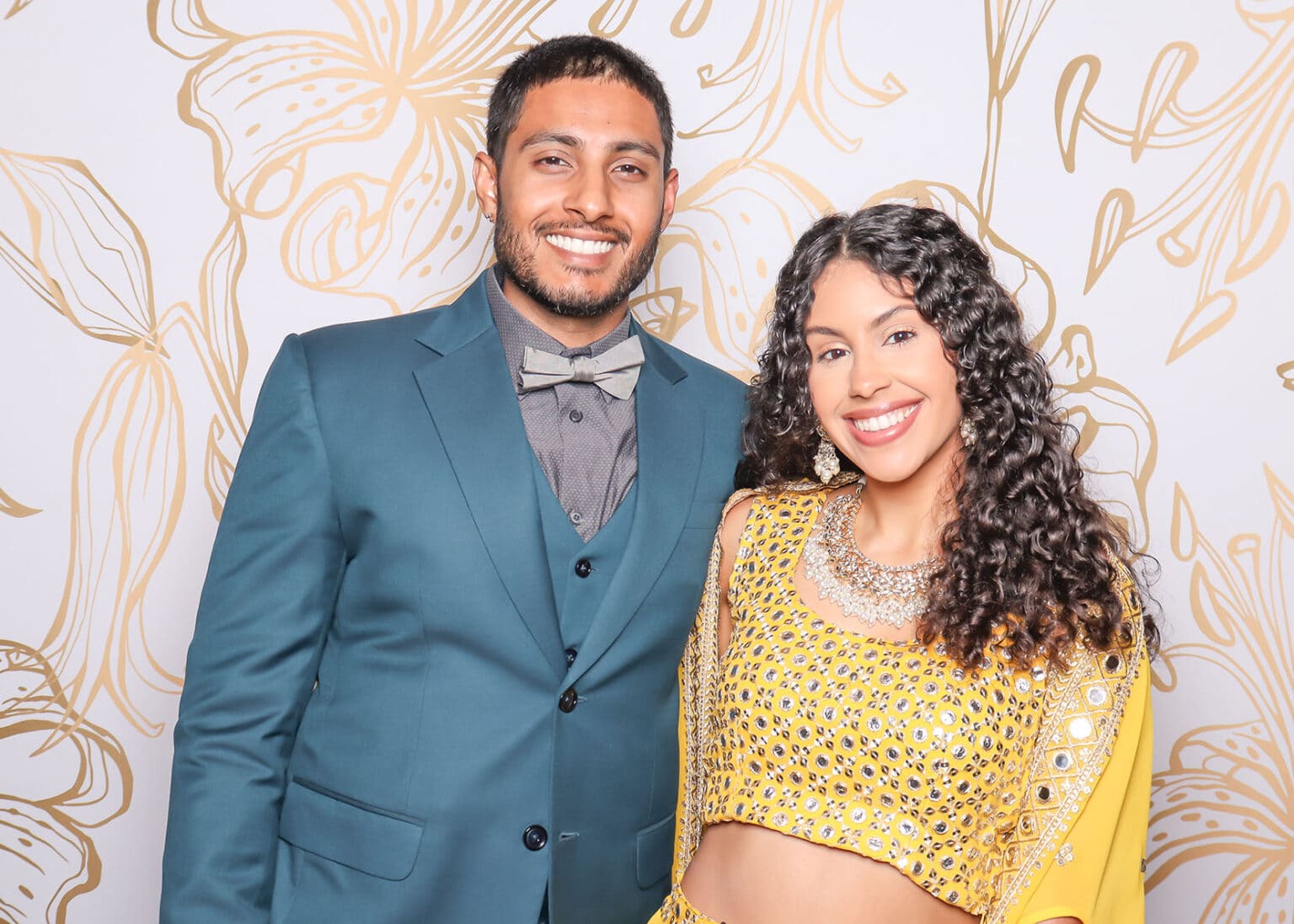 Couple posing at photo booth with gold floral backdrop and custom tension fabric design.