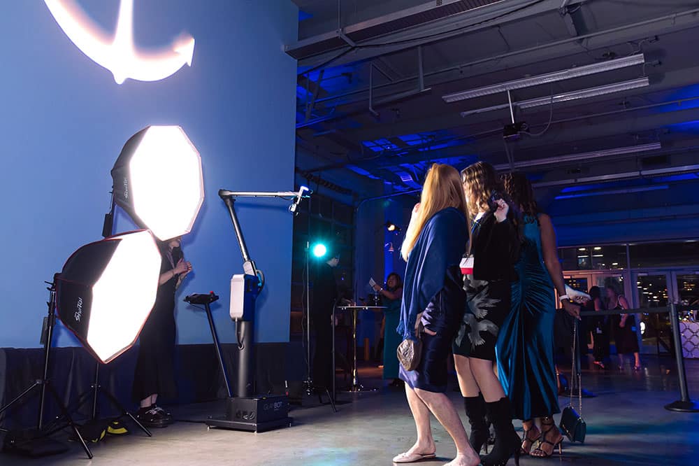 Group of guests posing in front of a photo booth setup with bright lighting and a stylish backdrop, highlighting a modern photo activation experience for events.