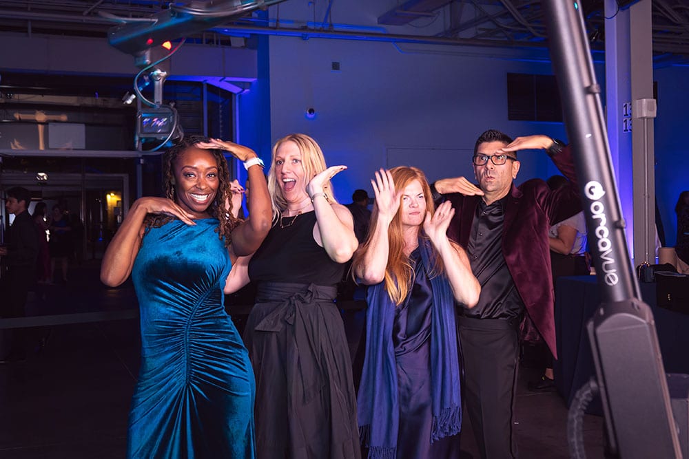 Group of four smiling individuals posing playfully in a vibrant event space with blue lighting, showcasing a lively atmosphere ideal for photo booth engagement at corporate and social events.