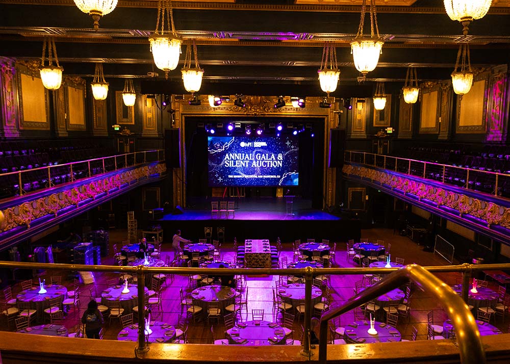 Interior view of The Regency Ballroom set for a corporate event, featuring round tables with glowing centerpieces and a stage displaying "Annual Gala & Silent Auction" banner, highlighting the venue's suitability for corporate gatherings.