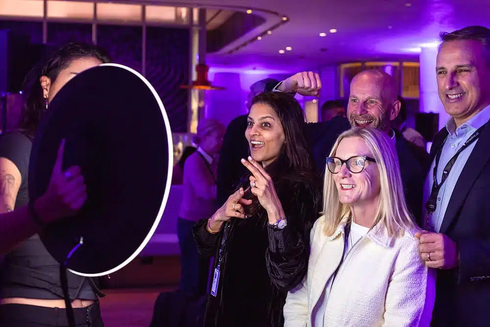 Group of four people enjoying a photo booth experience at a corporate event, with a glowing circular backdrop, capturing moments of engagement and excitement.
