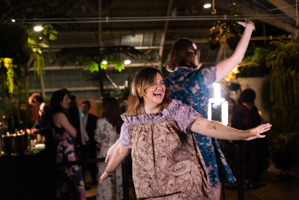Guests enjoying the 360 Video Booth experience, dancing and interacting in a lively event setting, surrounded by greenery and illuminated by soft lighting.