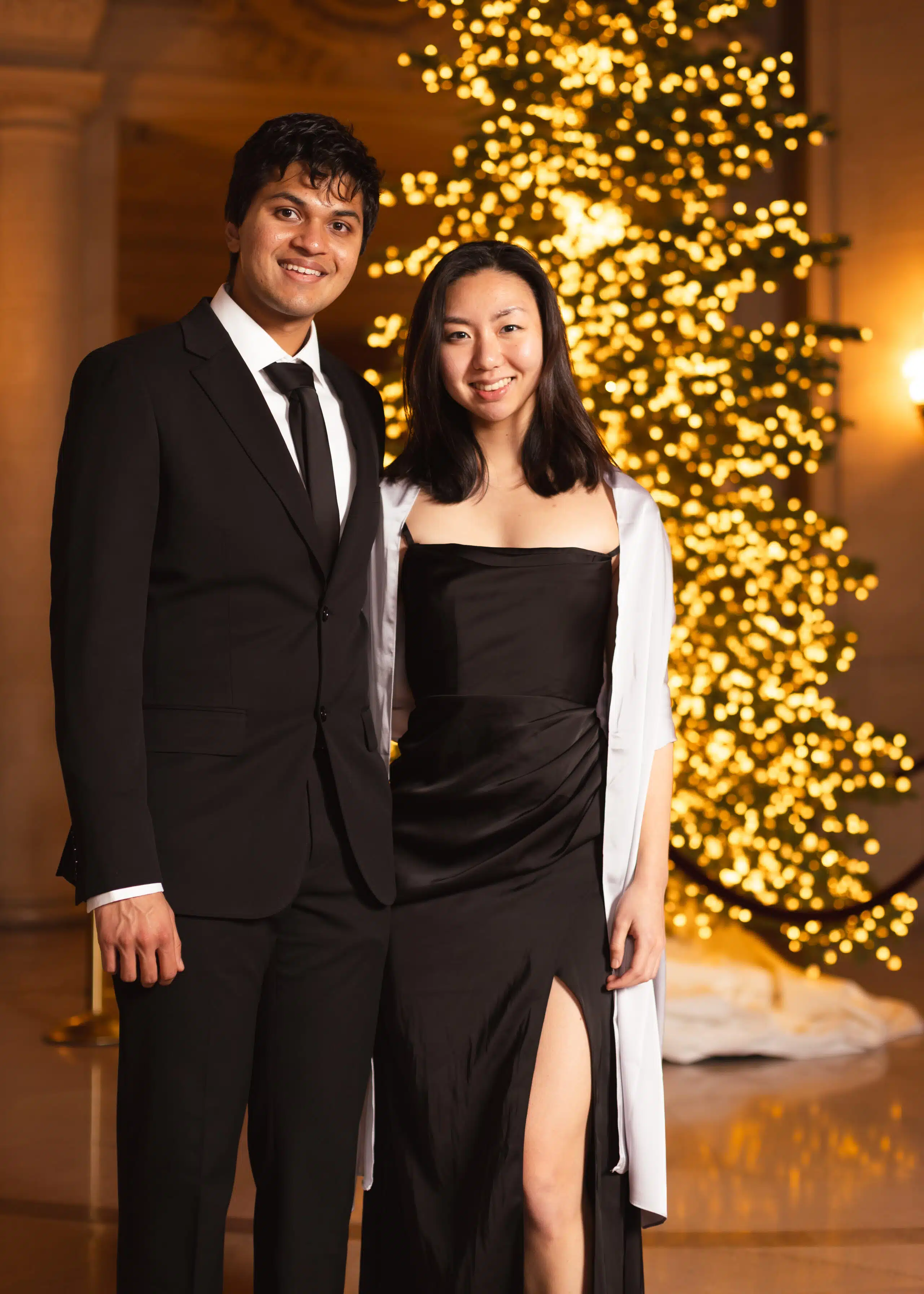 Couple in elegant attire posing for a portrait with a festive backdrop of twinkling lights, highlighting the luxury event atmosphere of Pop Life Photo's portrait studio experience.
