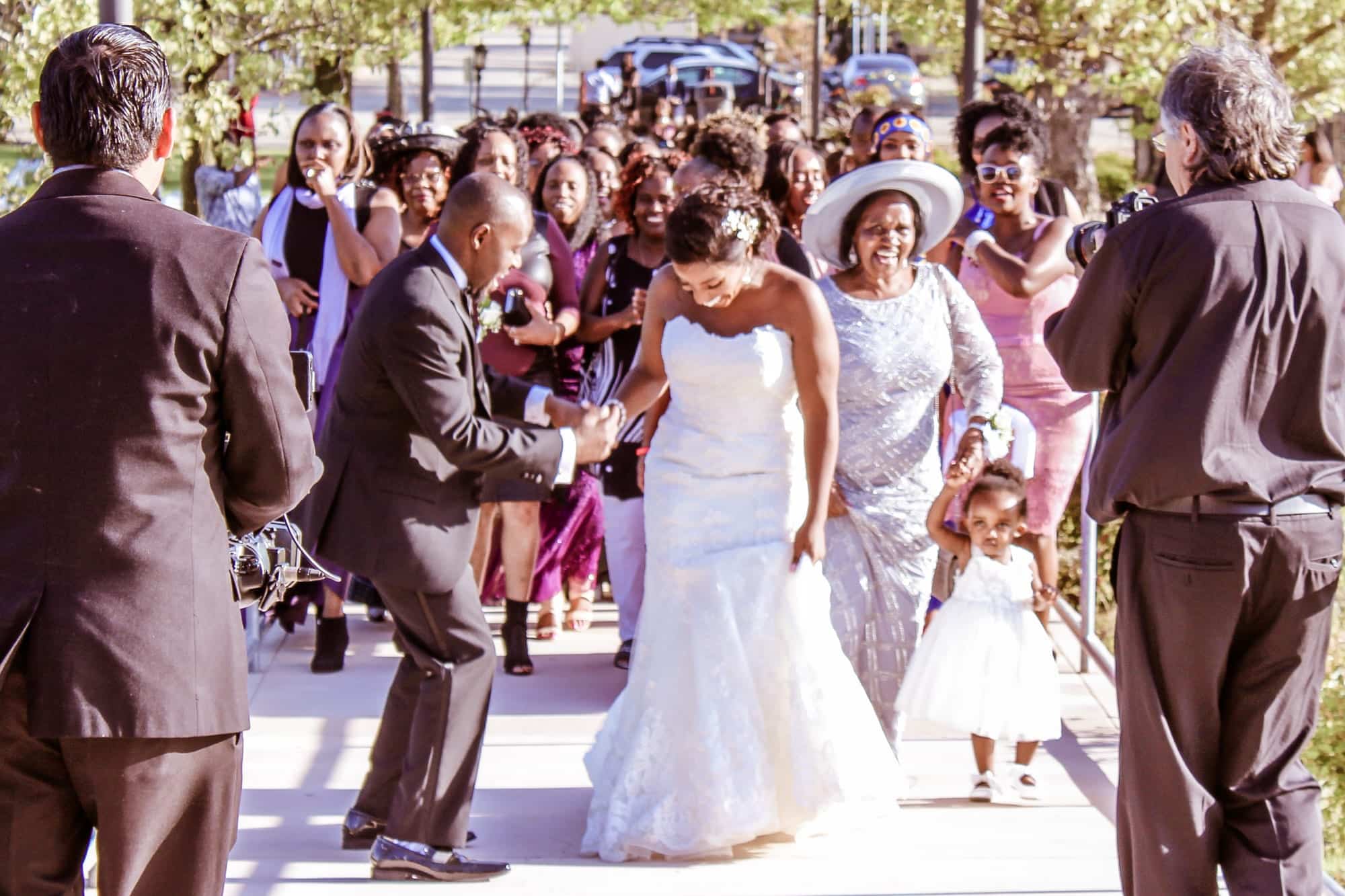 Bride in white gown smiling and walking down the aisle, accompanied by guests celebrating, capturing joyful moments at a Santa Clara event.