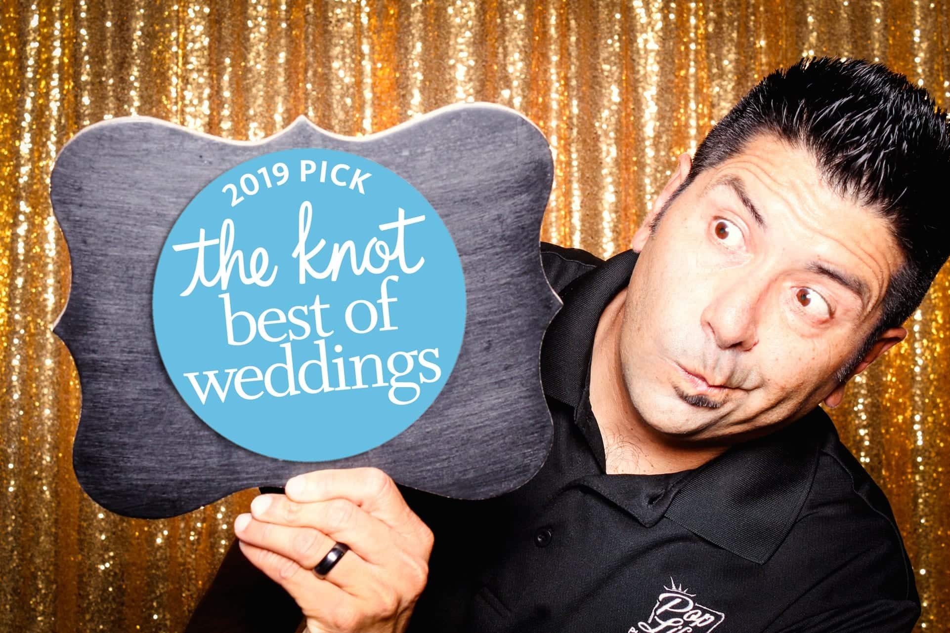 Man holding a sign that reads "2019 Pick the Knot Best of Weddings" in front of a golden sequin backdrop, showcasing Pop Life Photo's award-winning photo booth services for memorable events in Burlingame.