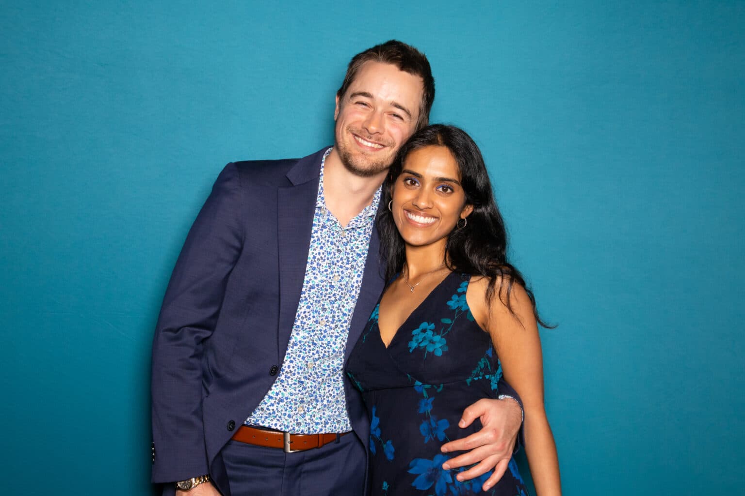 Couple smiling in front of a Deep Sea Blue photo booth backdrop