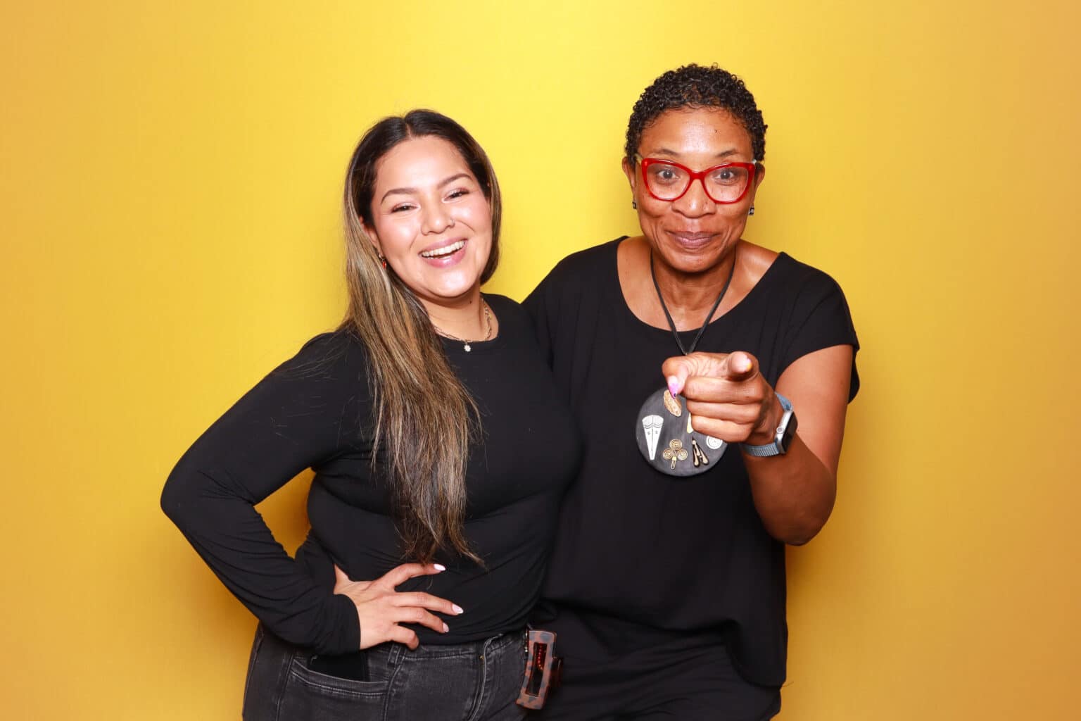 Two women smiling in front of a vibrant yellow photo booth backdrop, showcasing a polished