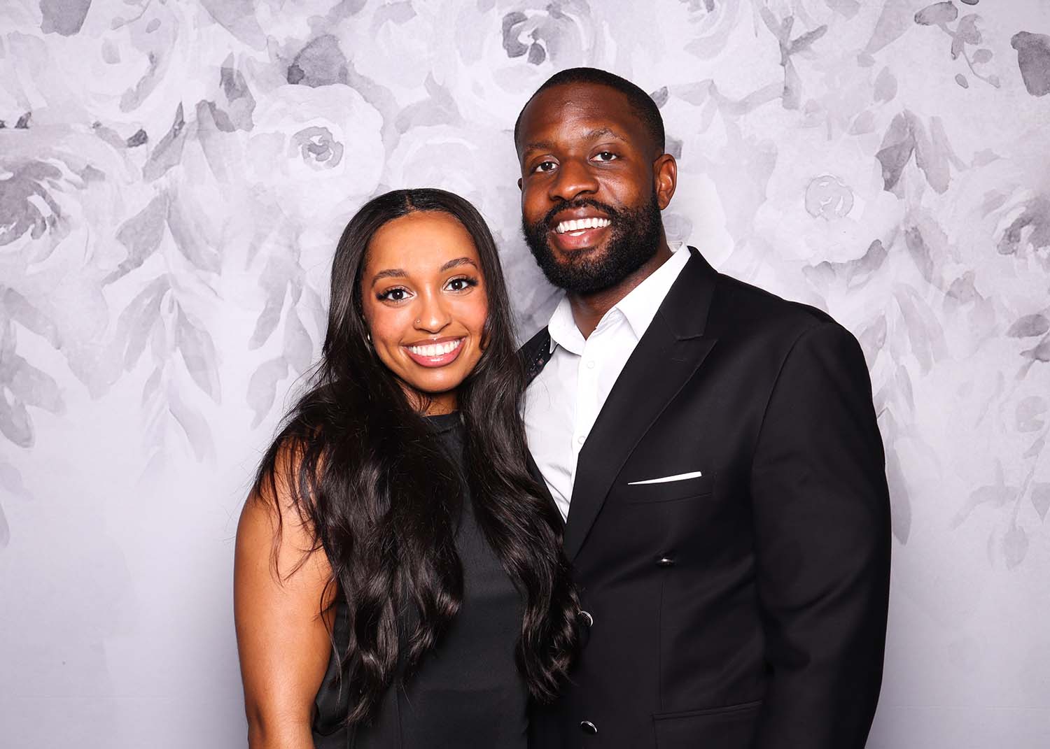 Couple posing happily in front of a gray floral backdrop, showcasing a sleek and elegant photo booth setting.