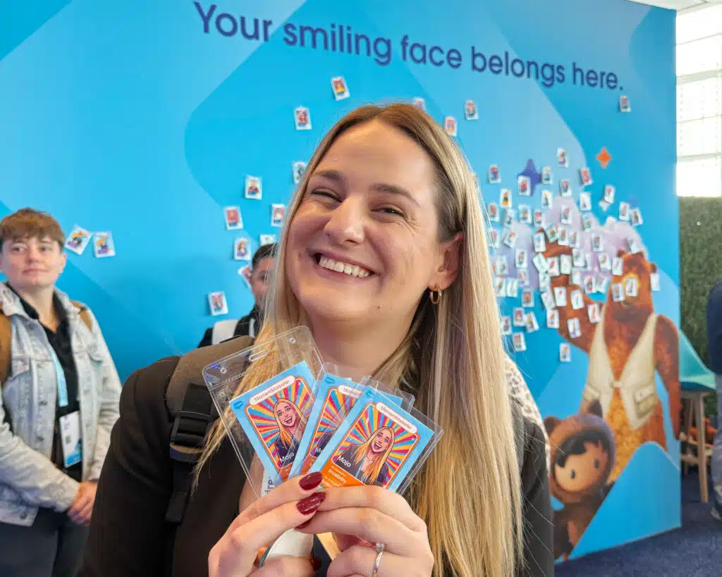 Smiling woman holding AI trading cards in front of a blue backdrop with the phrase "Your smiling face belongs here," showcasing engagement at Dreamforce event.