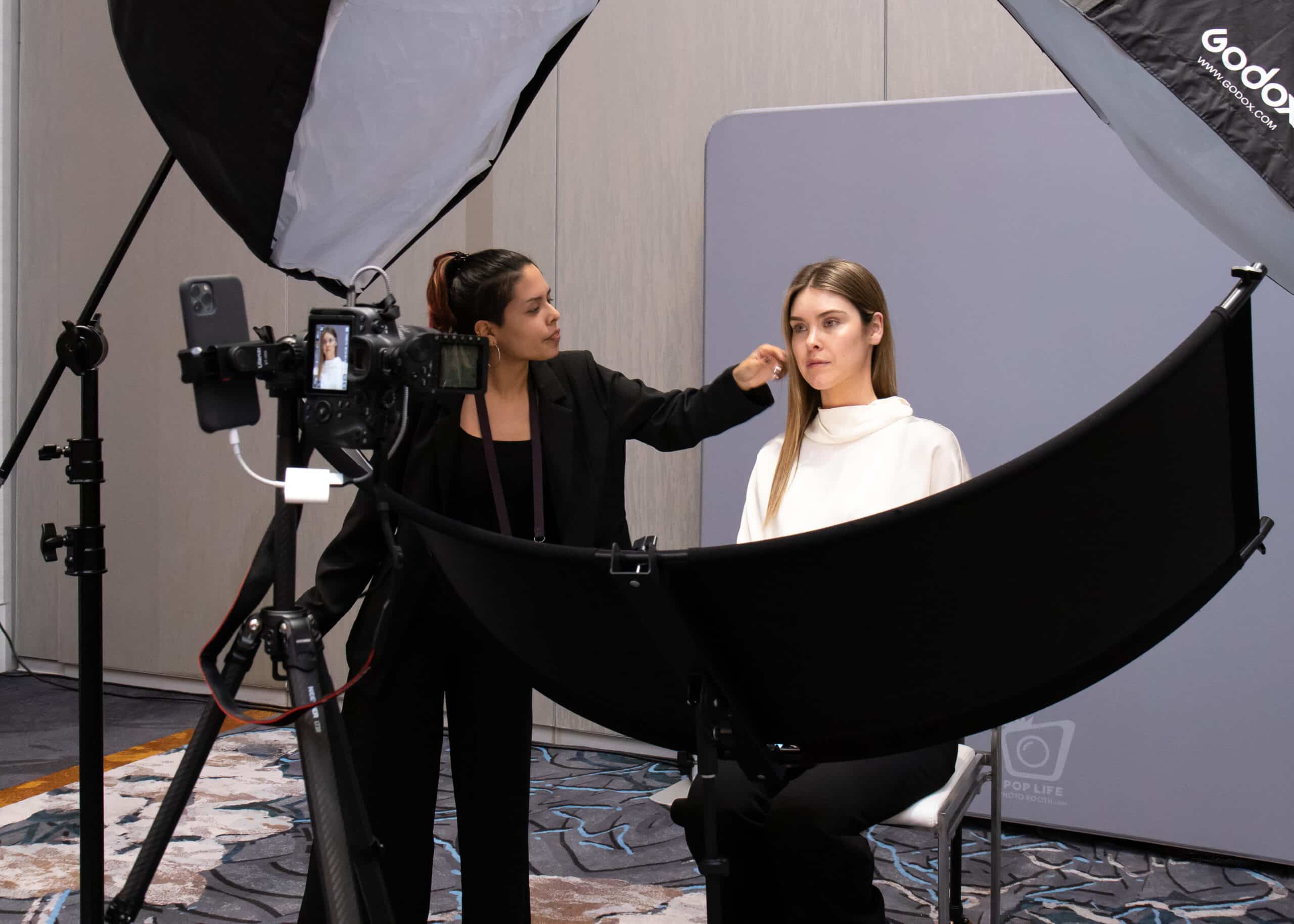 Professional photographer adjusting hair of a model in a studio setting, highlighting headshot photography services by Pop Life Photo during a corporate event.