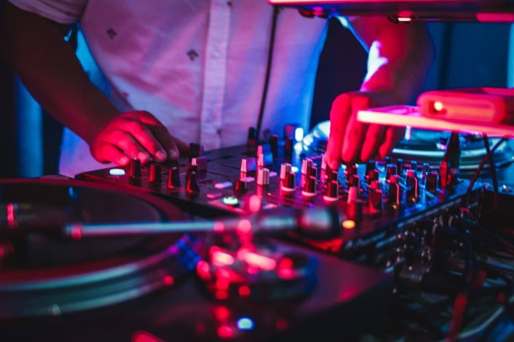 DJ mixing music on turntables and mixer in vibrant blue and red lighting, showcasing essential equipment for events.