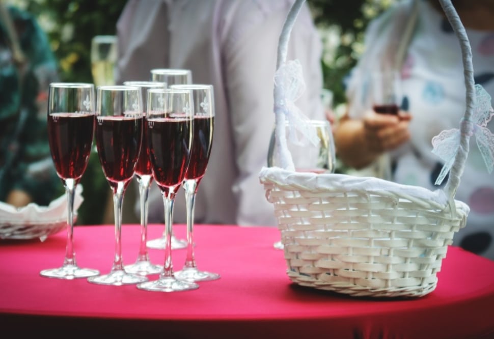 Glasses of red wine on a table with a white basket, symbolizing wine selection for weddings.