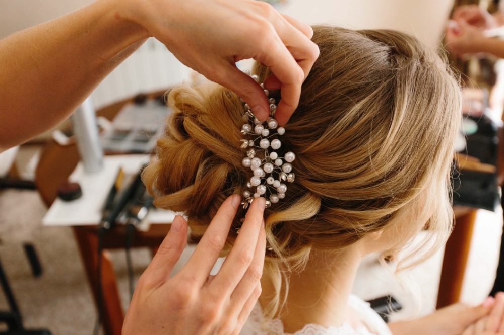 Bride's hair being styled with a decorative hairpiece, showcasing elegant wedding hairstyle preparation in a cozy setting.