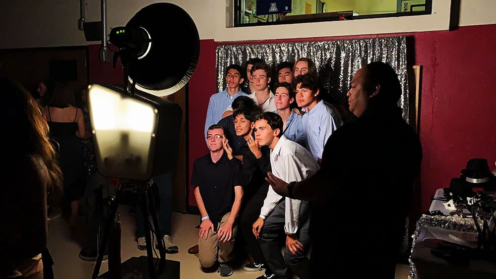 Group of students posing in front of a photo booth at a school event, with a spotlight illuminating them and a silver backdrop.