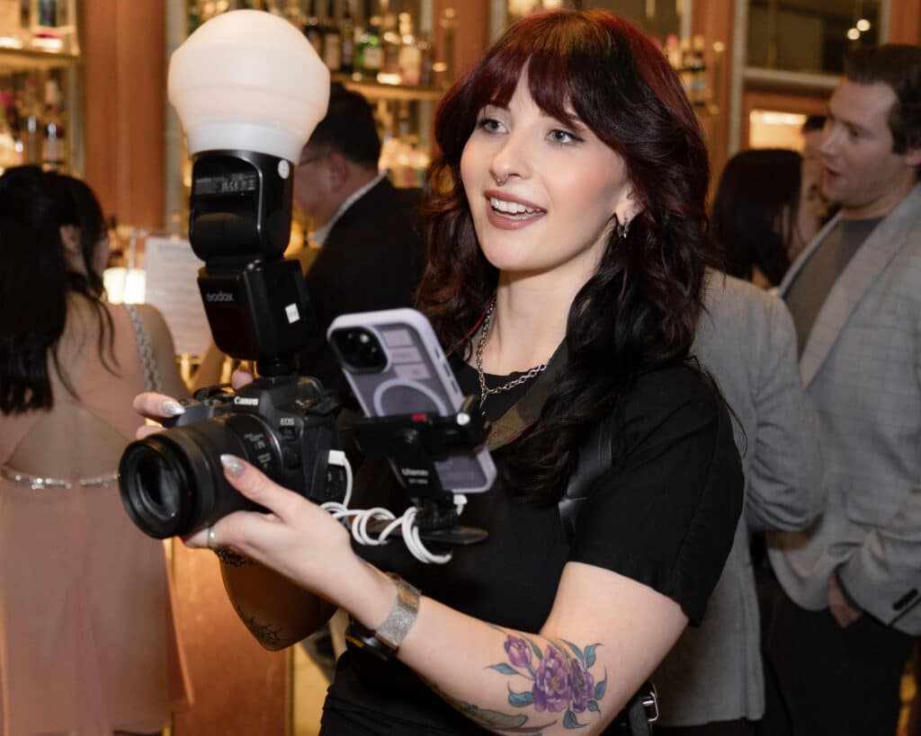 Photographer holding a camera with flash at a lively event, capturing candid moments and enhancing guest engagement.
