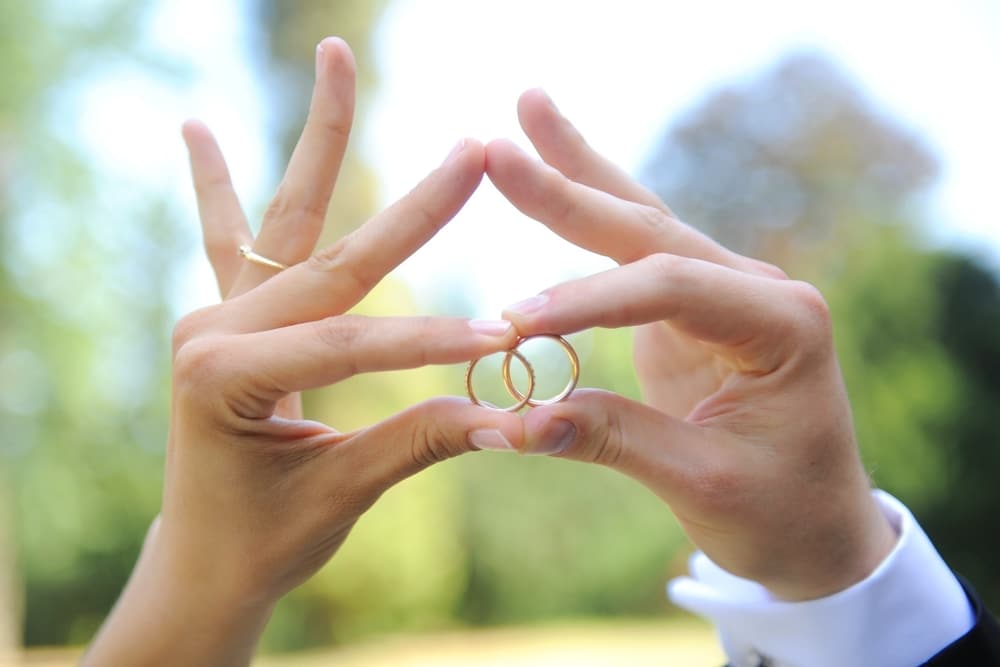 Couple's hands holding wedding rings outdoors, symbolizing love and commitment, relevant to wedding planning and photo booth experiences.