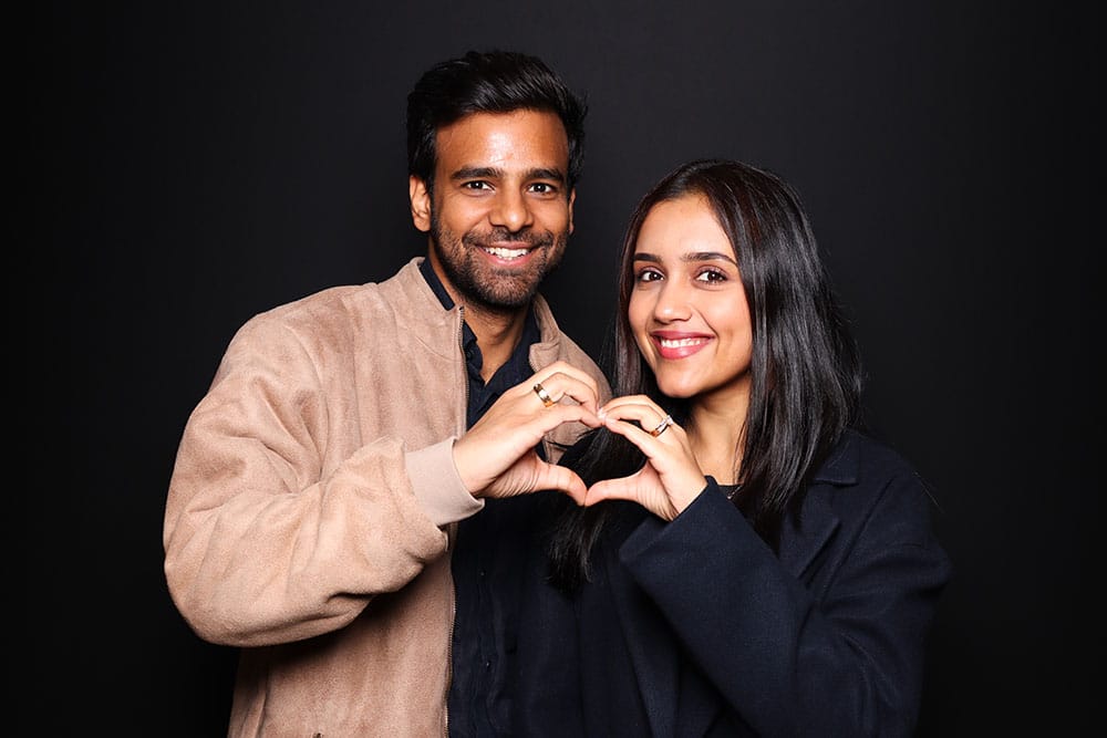 Couple making a heart shape with hands against a black backdrop, showcasing joyful connection and love, ideal for photo booth pose inspiration.