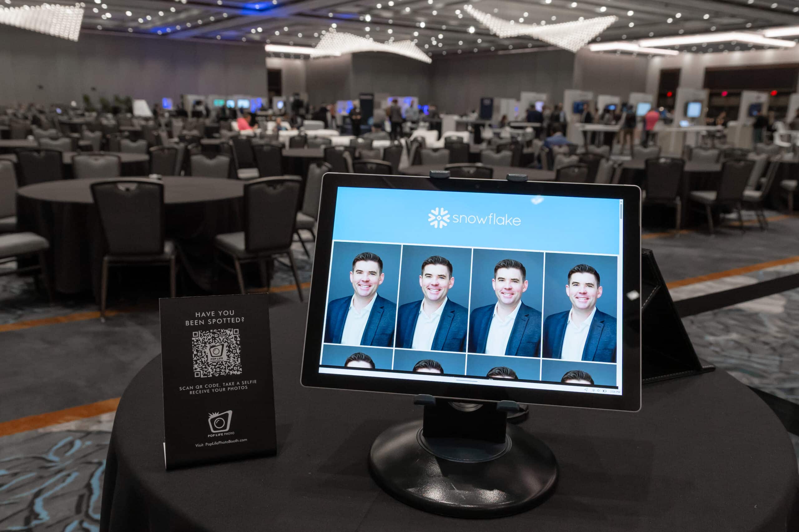 Display of headshot photos on a monitor for Snowflake at a corporate event, featuring a smiling man in a blazer, with a QR code sign inviting attendees to access their photos.