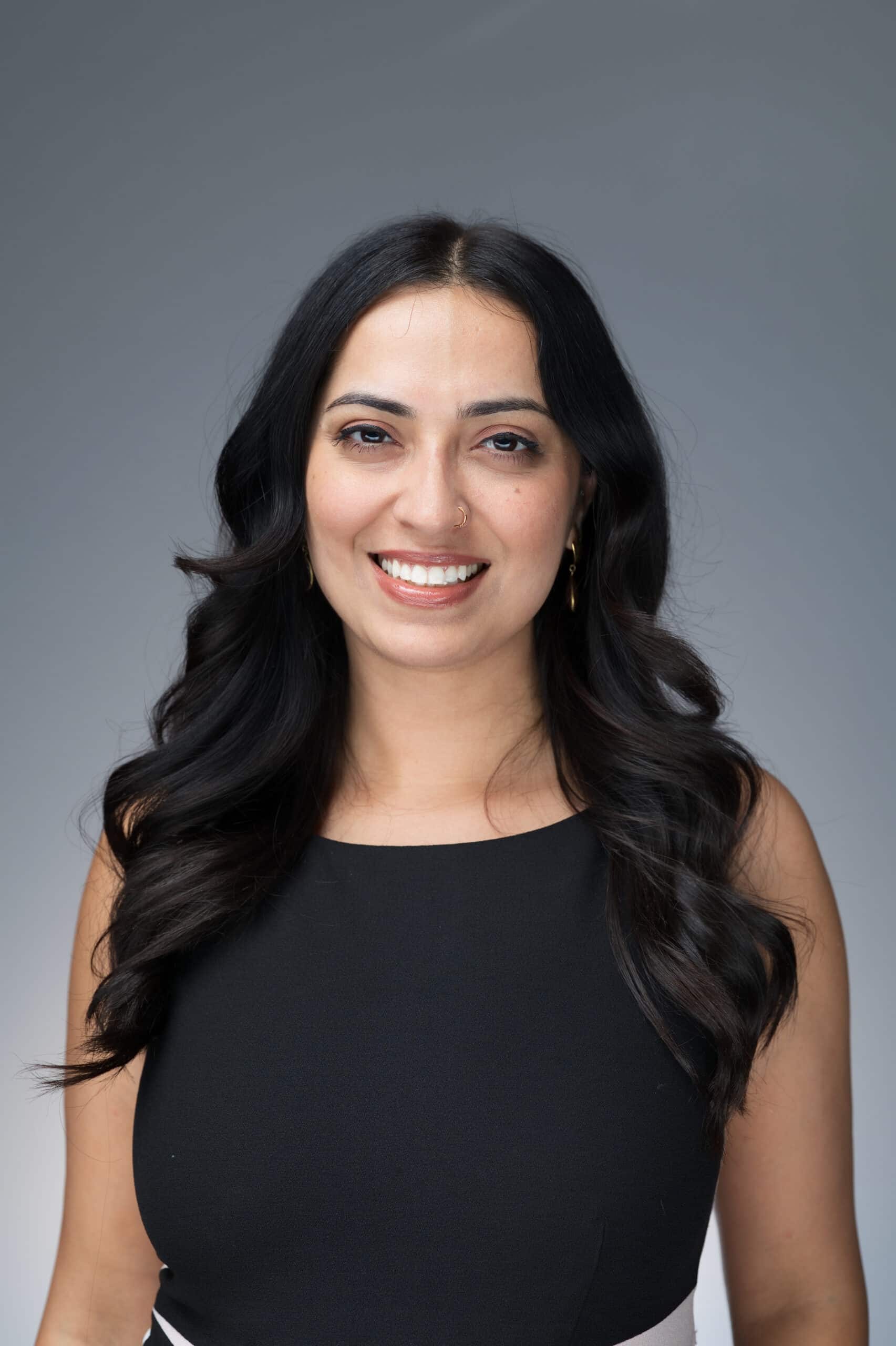 Professional headshot of a woman with long dark hair, wearing a black dress, smiling against a neutral gray background, showcasing Pop Life Photo's photography services at the Snowflake AI Innovation Summit.