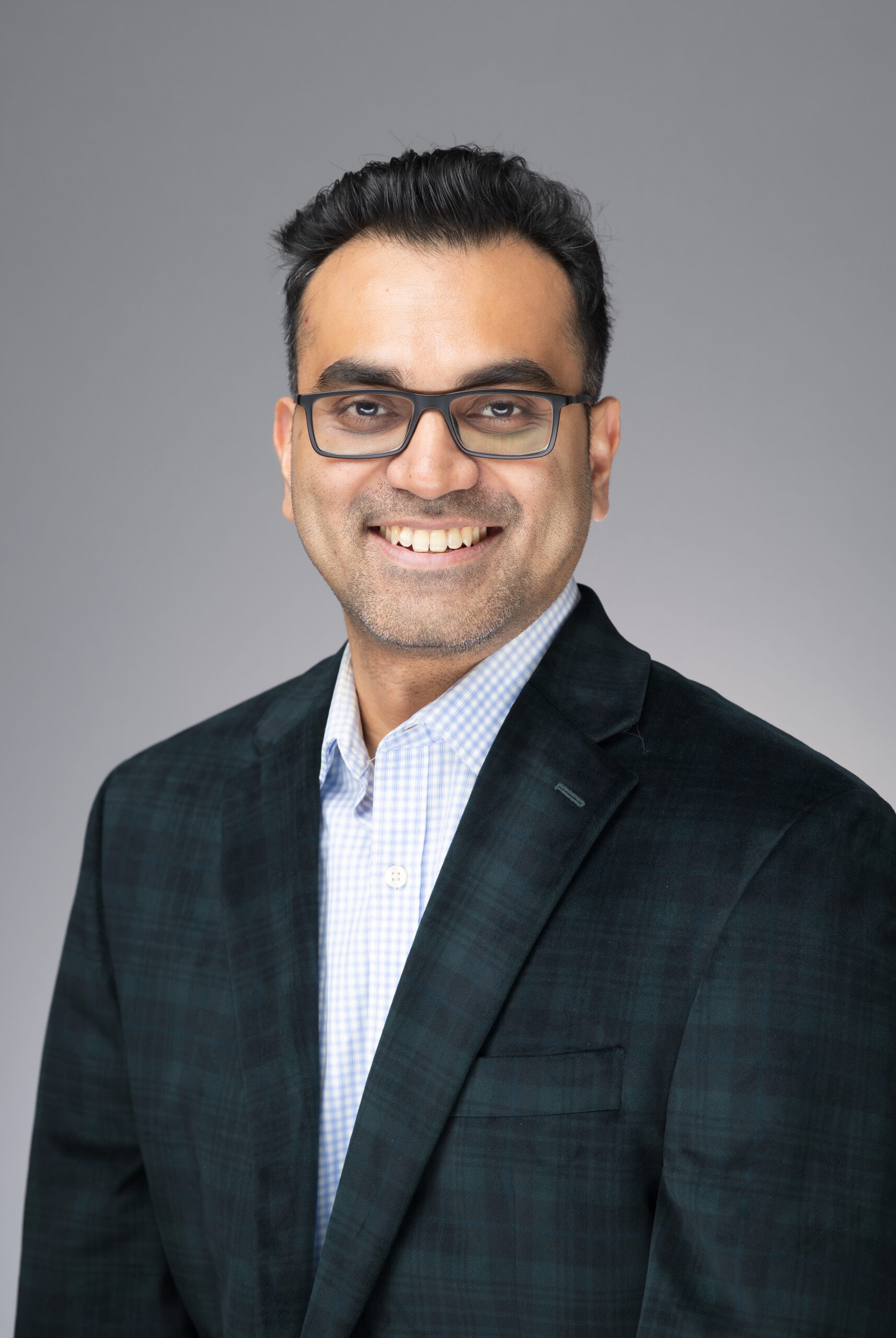 Professional headshot of a smiling man wearing glasses and a dark plaid blazer over a light checkered shirt, taken at the Snowflake AI Innovation Summit by Pop Life Photo.