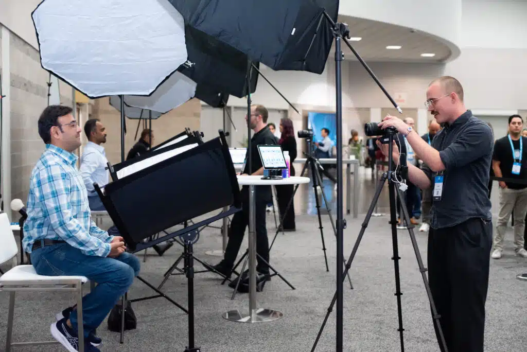 Professional headshot photography setup at corporate event, featuring photographer capturing images of employee in front of lighting equipment and backdrop.