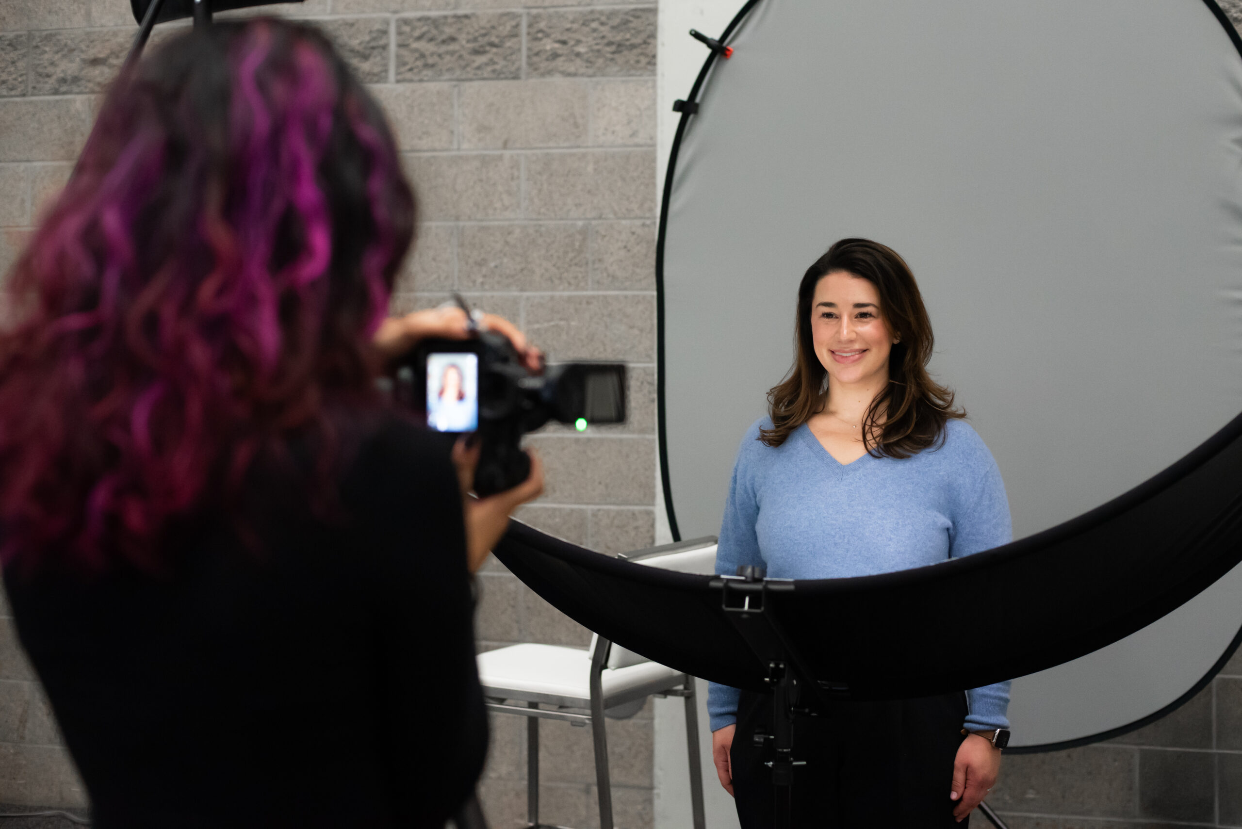 Professional headshot session at Snowflake AI Innovation Summit, featuring a woman smiling in front of a photography backdrop, while a photographer captures her image with a camera.