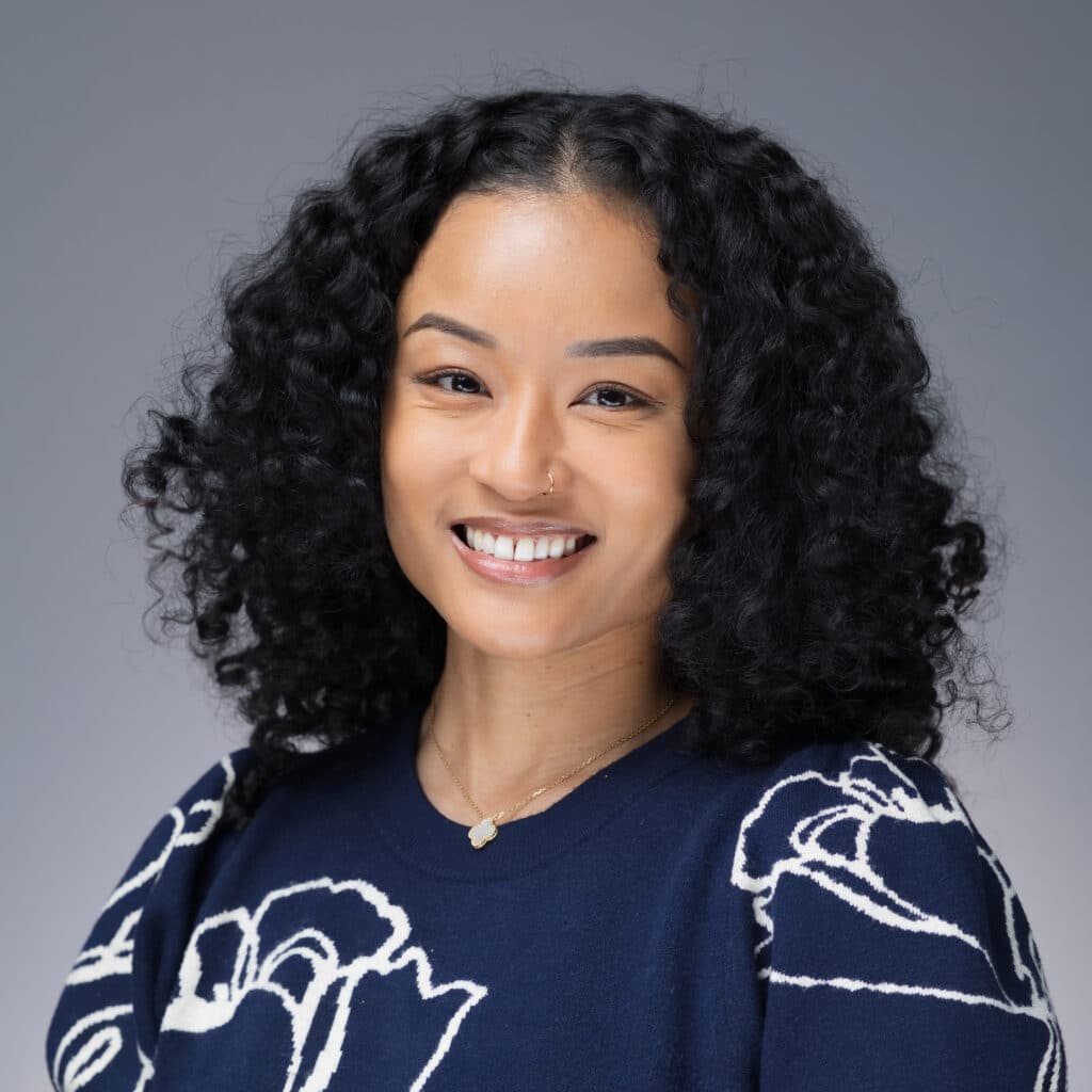 Smiling woman with curly hair wearing a navy sweater featuring floral design, representing professional employee headshots for company culture.
