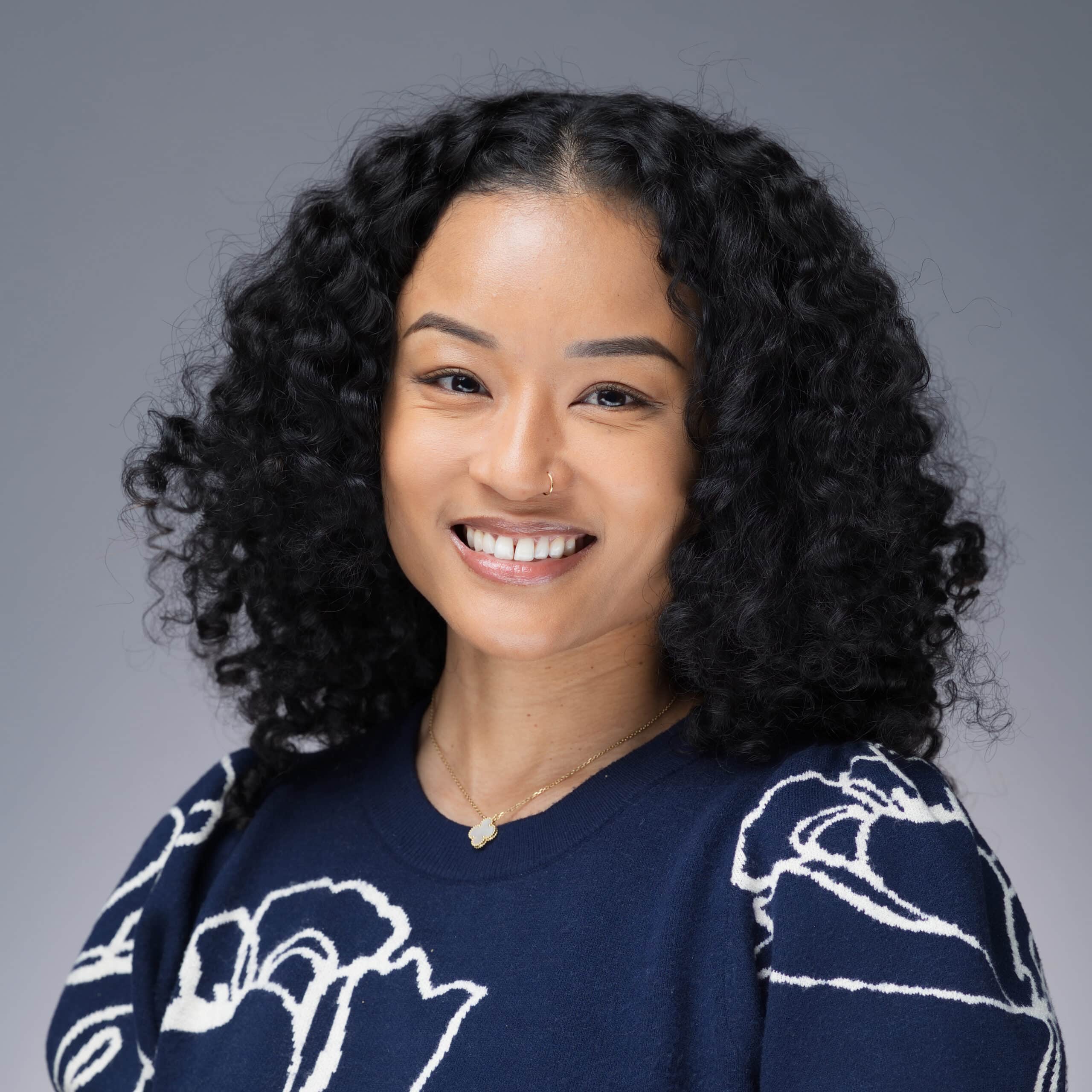 Smiling woman with curly hair wearing a navy sweater featuring floral design, representing professional employee headshots for company culture.