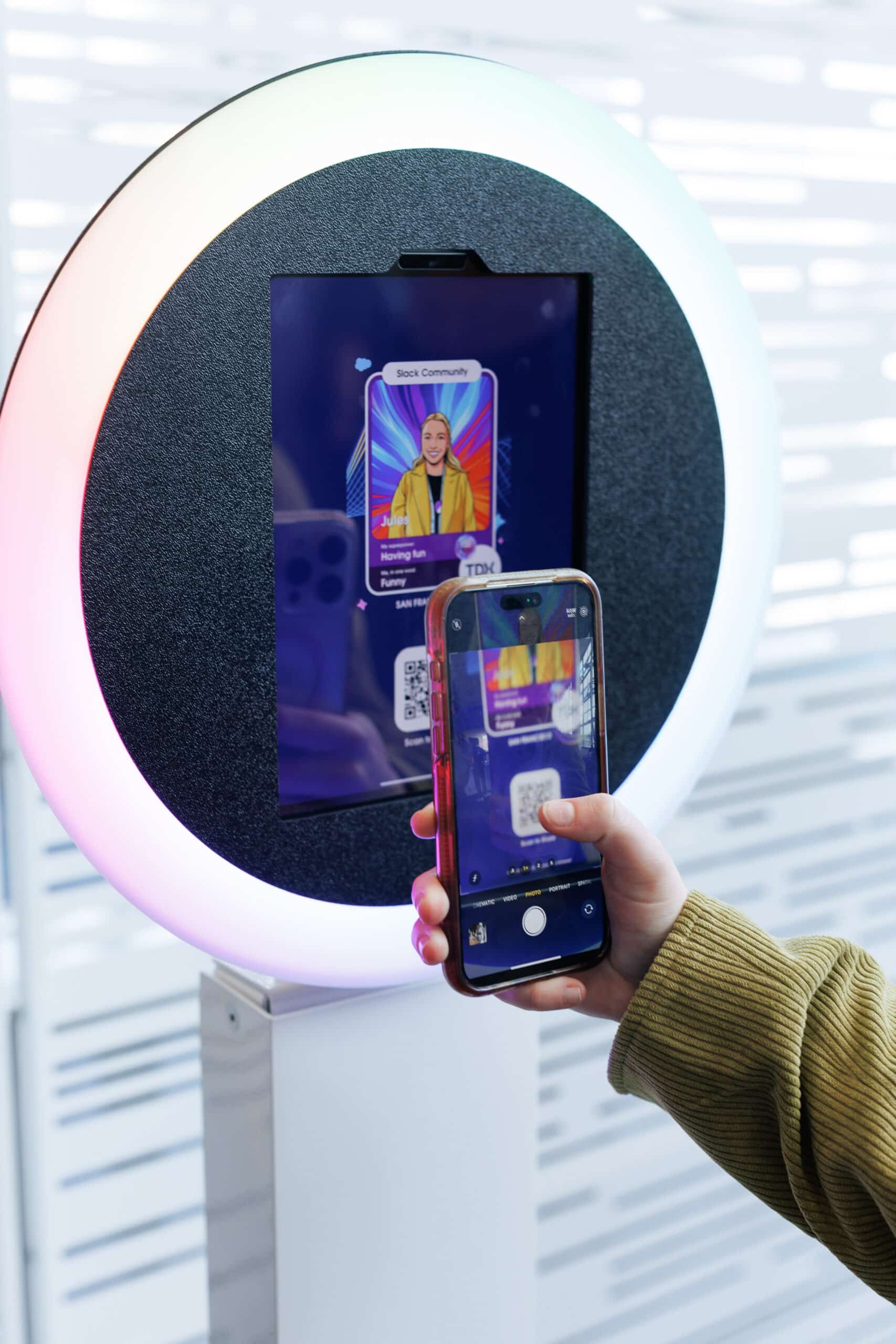 Person using smartphone to scan QR code on digital display of custom illustrated character at Salesforce TDX 2026 event, showcasing Pop Life Photo's AI Trading Card activation.