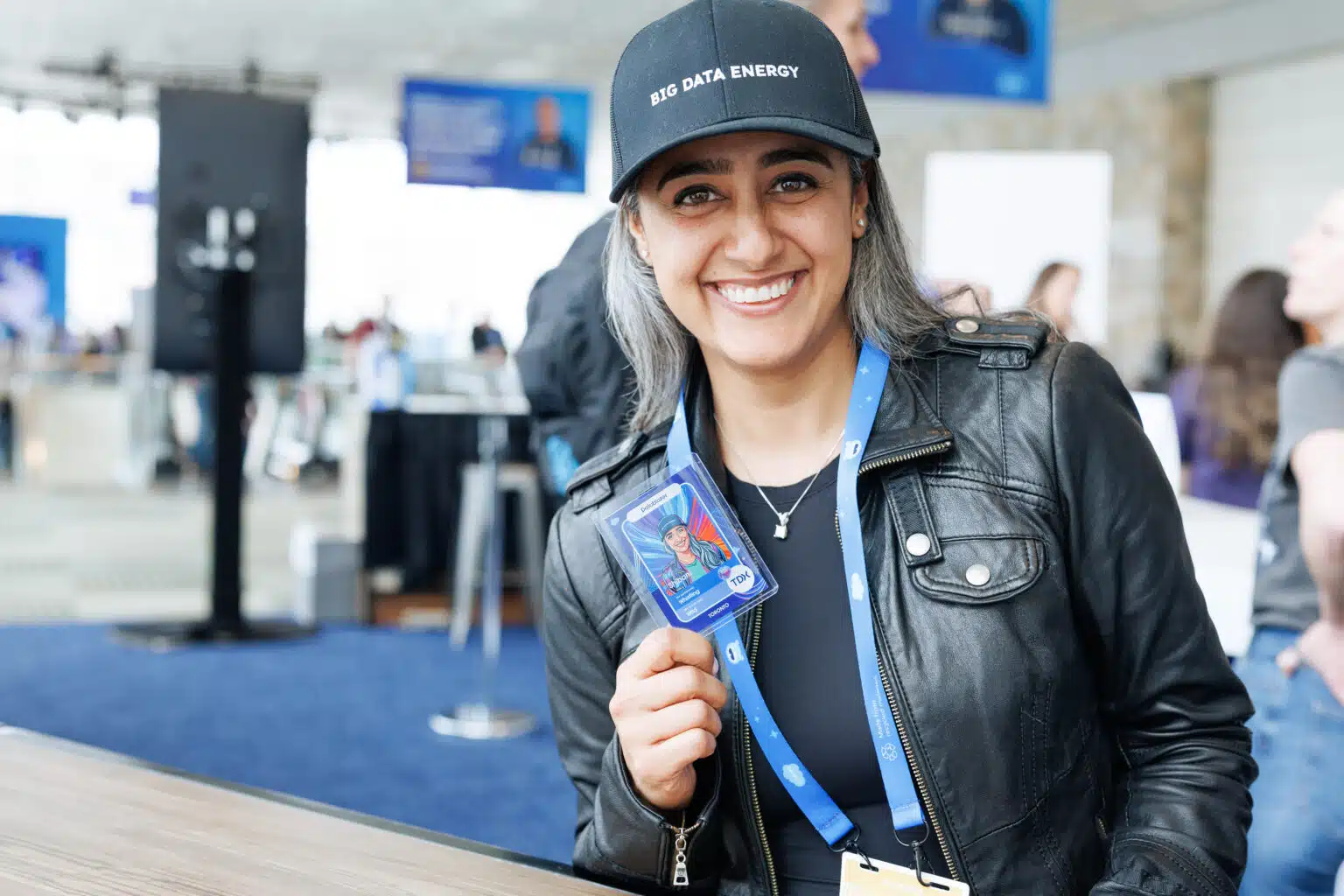 Smiling woman wearing a "BIG DATA ENERGY" cap, holding an AI-generated trading card at a corporate event, showcasing personalized guest experiences and brand engagement.