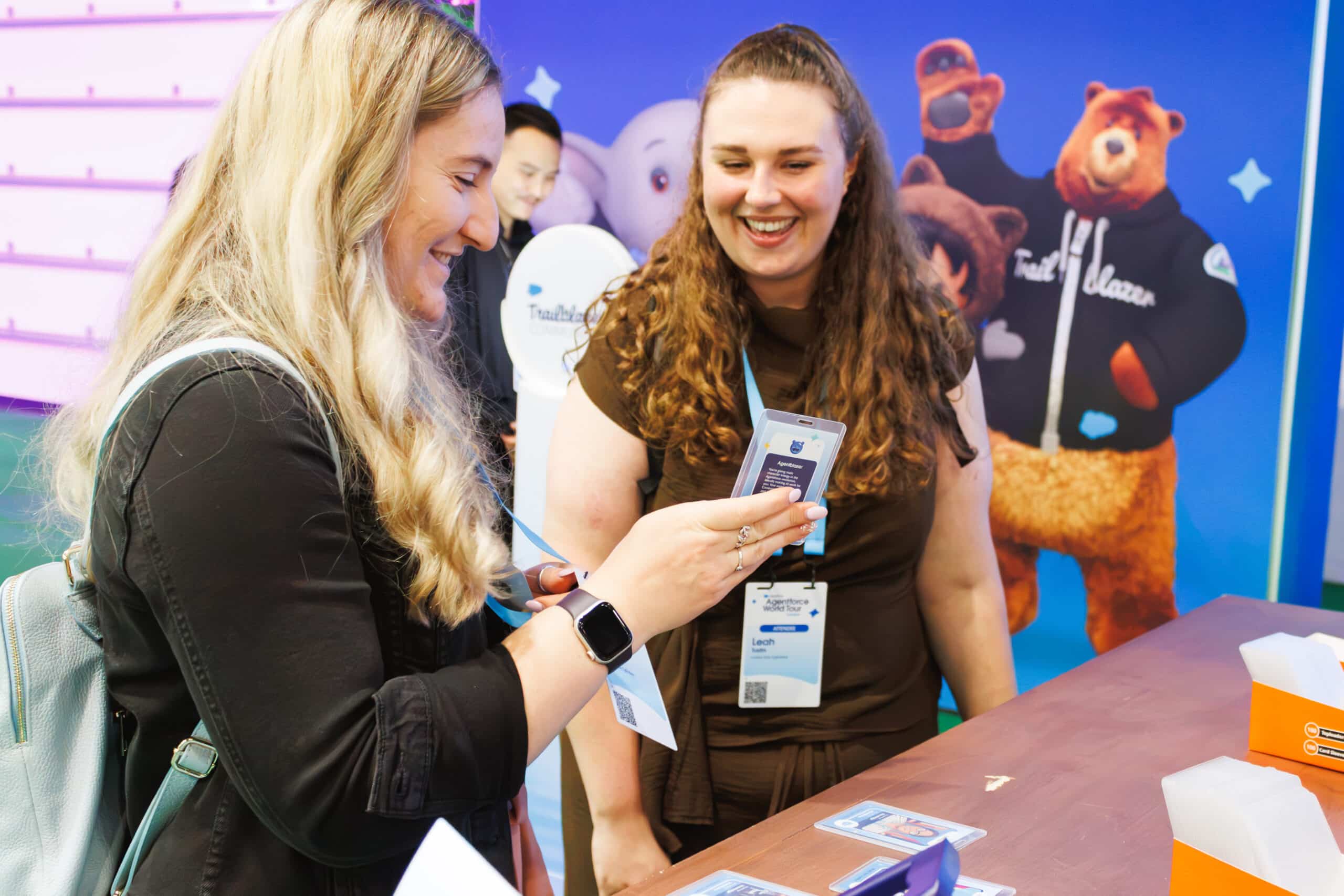 Two women smiling and viewing AI trading card activation at Salesforce World Tour London event.
